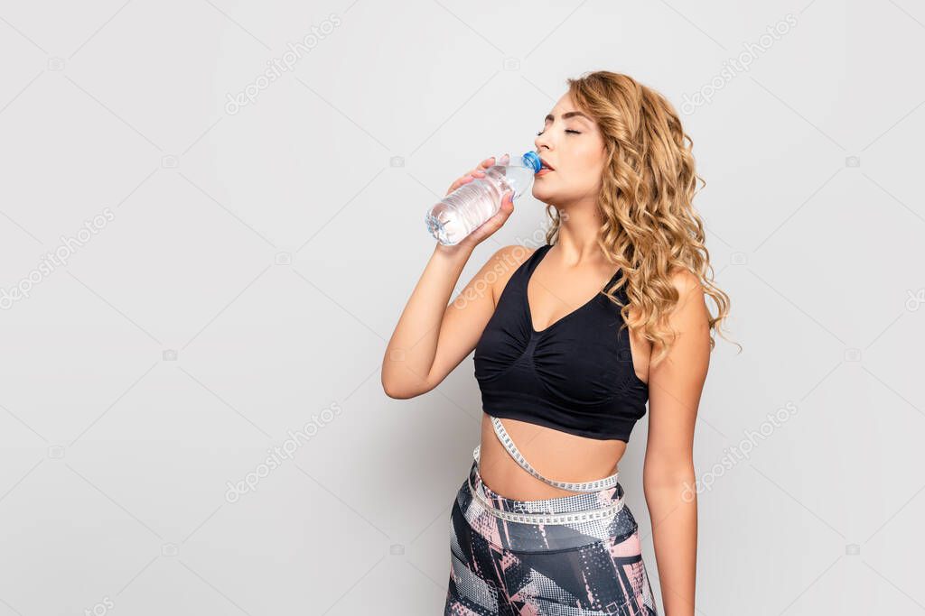 Younf sportswoman drink water from a bottle after exercise for a healthy life and measuring her waist with tape measure