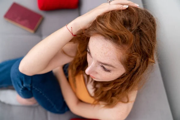 Triste joven está sentada en el sofá puso su mano sobre su cabeza mientras pensaba. — Foto de Stock