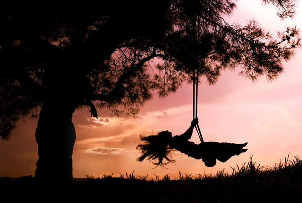 Silhouette of happy young woman on a swing with sunset background Stock Image