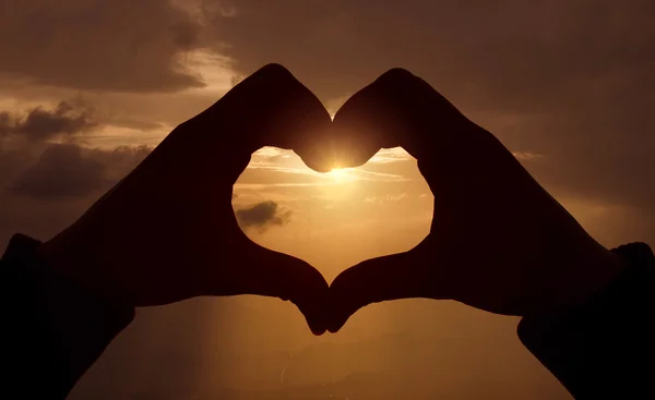 Forma do coração com as mãos no pôr do sol — Fotografia de Stock