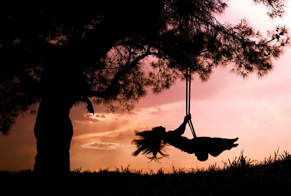 Sylwetka szczęśliwej młodej kobiety na huśtawce z zachodem słońca — Zdjęcie stockowe