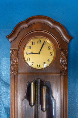 Vintage Wooden Pendulum Clock Against Blue Wall. High quality photo