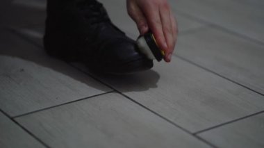 Adam loş ışıkta siyah ayakkabıları temizliyor.