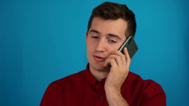 Um homem está falando ao telefone em um fundo azul — Vídeo de Stock