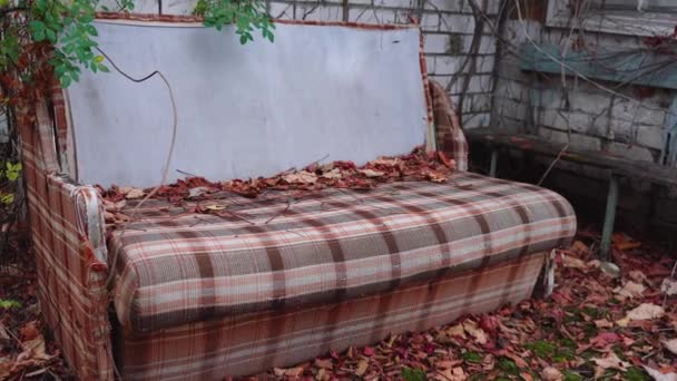 Un viejo sofá se encuentra en la calle cerca de una casa abandonada — Vídeo de stock