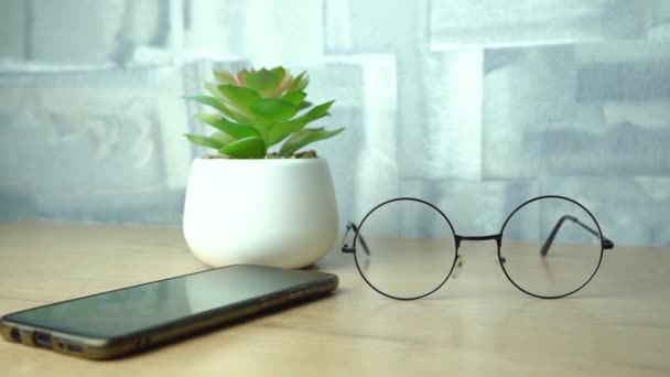 Phone, flower and glasses are on the wooden table — Video Stock