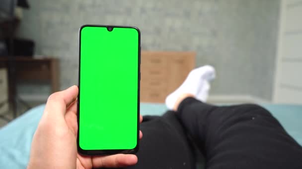 Людина використовує телефон з зеленим екраном лежить на ліжку — стокове відео
