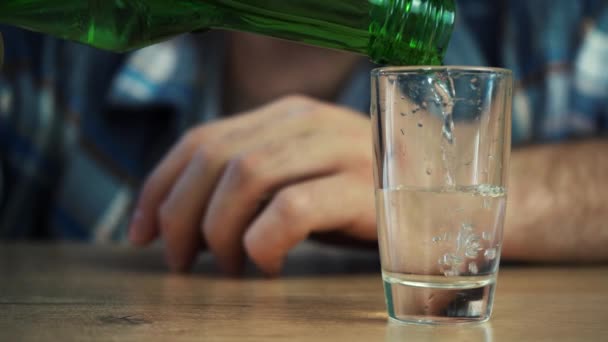 Een alcoholist schenkt een glas wodka in terwijl hij aan tafel zit en drinkt het — Stockvideo