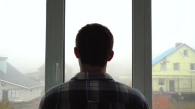 Sisli bir şehirde bir adam evinin penceresinden dışarı bakar.