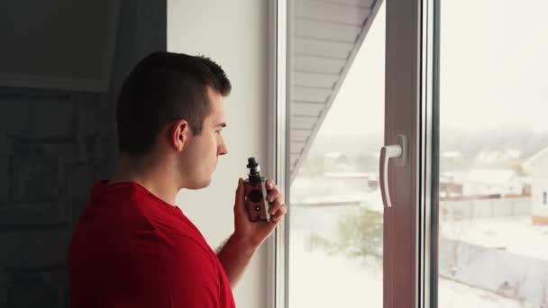 माणूस खिडकीतून व्हेप धूम्रपान करतो — स्टॉक व्हिडिओ