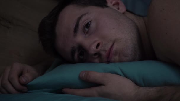 Чоловік лежить на ліжку і не може заснути, страждаючи від безсоння — стокове відео