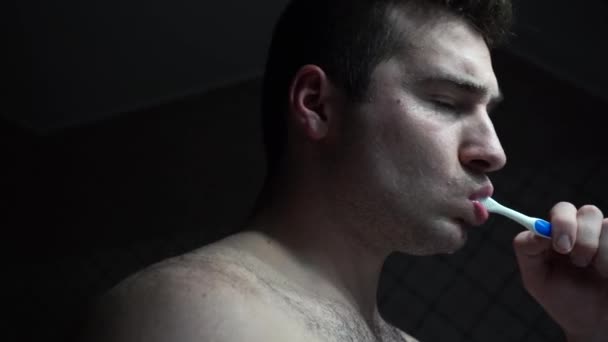 Un hombre se cepilla los dientes con la tenue luz del baño — Vídeos de Stock