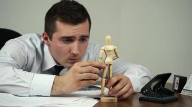 Erkek ofis çalışanı iş yerinde tahta bebekle oynuyor.