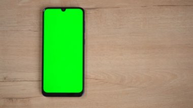 Ahşap bir masanın üzerinde yeşil ekranlı bir telefon var.