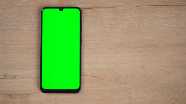 Egy zöld képernyős telefon fekszik egy fa asztalon — Stock videók