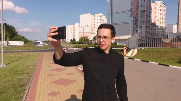 Een man neemt foto 's van zichzelf aan de telefoon die door de stad loopt — Stockvideo