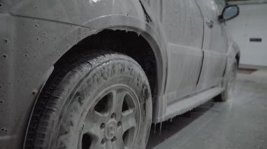 Bir adam araba yıkama yerindeki bir arabaya köpük sürer.