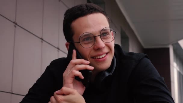 Jovem falando ao telefone enquanto sentado na rua — Vídeo de Stock