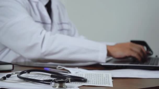Лікар друкує в ноутбуці, сидячи в своєму офісі. концепція медицини — стокове відео