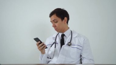 Doktor ofiste otururken telefonu kullanıyor.