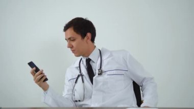 Doktor ofiste otururken telefonu kullanıyor.