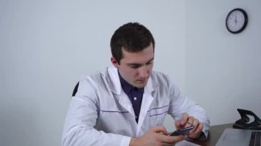 Doktor masada otururken telefonu kullanıyor.