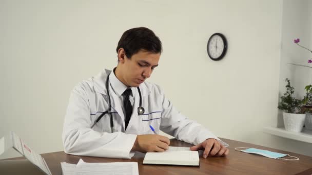 Лікар тримає документацію, сидячи за столом у своєму офісі — стокове відео