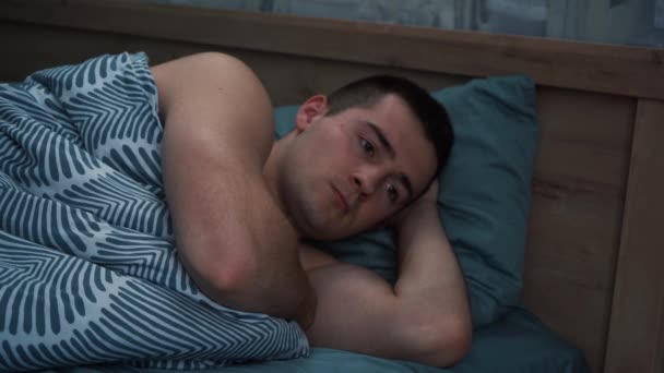 Un hombre que sufre de insomnio no puede dormir acostado en la cama — Vídeo de stock