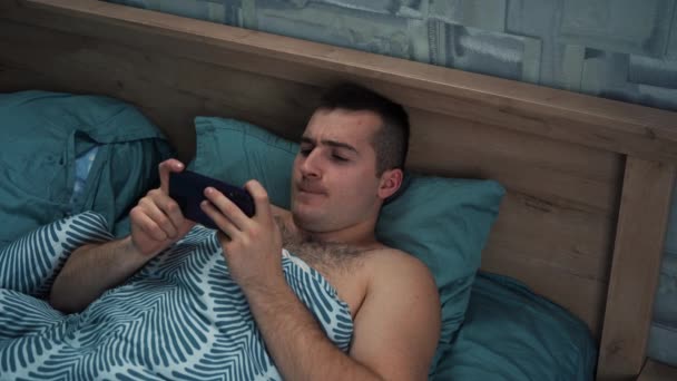 Un hombre jugando en el teléfono mientras está acostado en la cama — Vídeo de stock