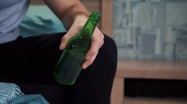 Kanepede oturan bir adam elinde yeşil cam şişeyle bira tutuyor..