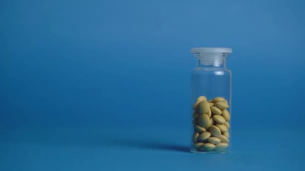 Стеклянная колба с таблетками лежит на голубом фоне — стоковое видео