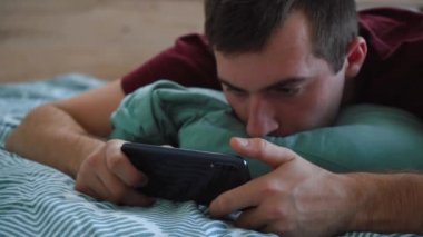 Adam yatakta yatarken telefon kullanıyor.