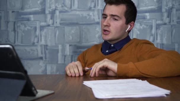 Um homem se comunica via comunicação por vídeo enquanto está sentado em uma mesa. — Vídeo de Stock
