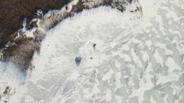 Человек сидит на льду и ловит рыбу рядом с палаткой. воздушная стрельба. — стоковое видео