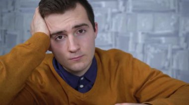 Yorgun adam masada otururken kameraya bakıyor.