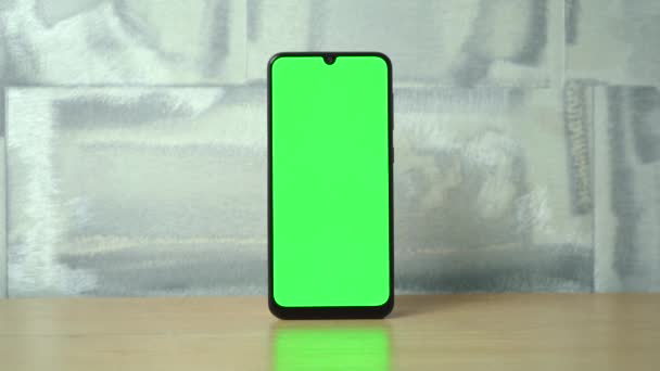 Telefon zöld képernyővel áll egy fa asztalon. — Stock videók