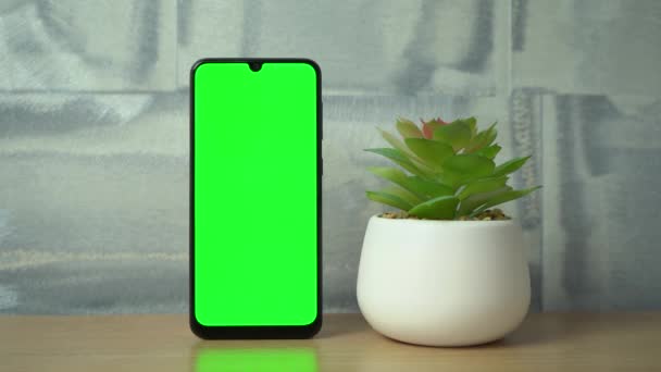 Vertikální telefon se zelenou obrazovkou stojí na stole vedle květiny — Stock video