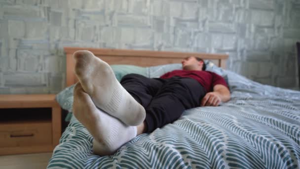 A man lies on the bed in dirty socks — Stock Video