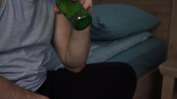 Mann trinkt Bier aus grüner Glasflasche, während er auf Sofa sitzt — Stockvideo