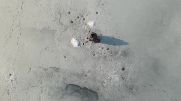 Pêcheur attrapant du poisson assis sur la glace de la rivière — Video