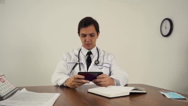 Mužský lékař hrát hry na telefonu na pracovišti — Stock video
