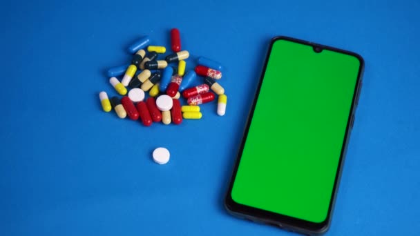 Pillen liggend op blauwe achtergrond met telefoon met groen scherm — Stockvideo