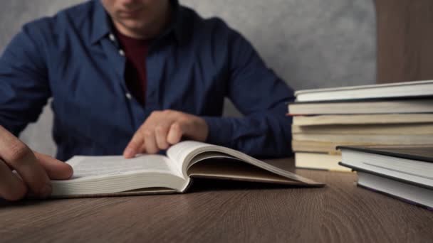 Egy férfi könyvet olvas, miközben az asztalnál ül. — Stock videók