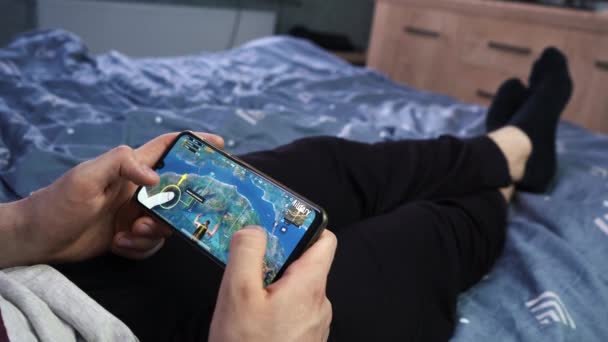 Mann spielt pubg am Telefon, während er auf dem Bett liegt. Moskau Russland 12. Mai 2021 — Stockvideo