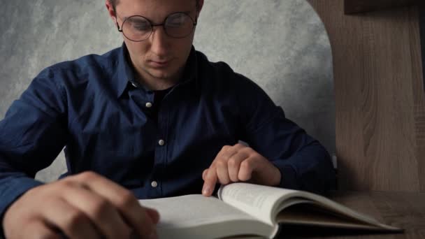 Un hombre leyendo un libro mientras está sentado en una mesa. — Vídeo de stock