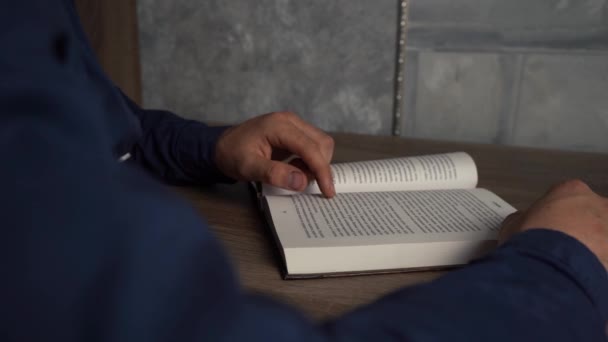 Egy férfi könyvet olvas, miközben az asztalnál ül. — Stock videók