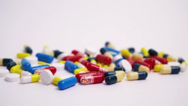 Un montón de píldoras de diferentes colores se encuentran sobre un fondo blanco — Vídeos de Stock