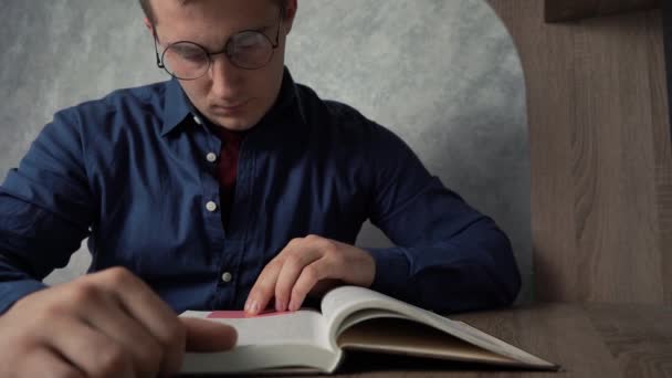 Egy férfi könyvet olvas, miközben az asztalnál ül.. — Stock videók