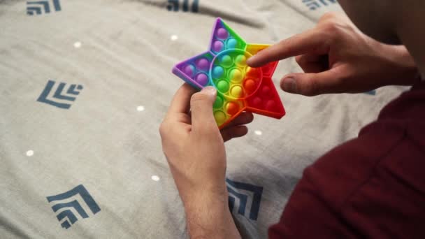 Guy playing pop it toy simple dimple in the shape of a star lying on the bed — Stok video