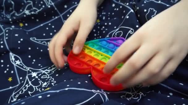 Κορίτσι παίζει ποπ παιχνίδι απλό λακκάκι κάθεται στο κρεβάτι — Αρχείο Βίντεο